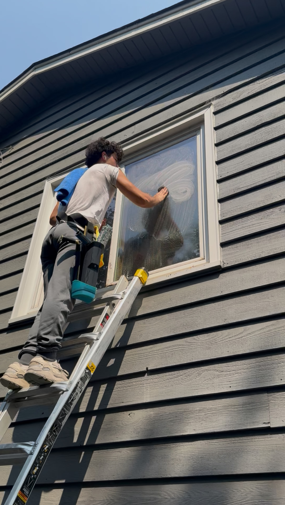 TurboClean Exteriors technician on a ladder squeegeeing a second-story window